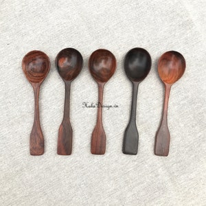 May include: Five wooden spoons with different wood grain patterns. The spoons are arranged in a row on a light grey fabric background.