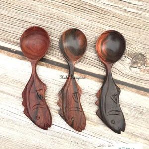 May include: Three wooden spoons with fish-shaped handles. The spoons are made of dark wood with a reddish hue. The fish handles are carved with details and have a black and brown colour scheme.