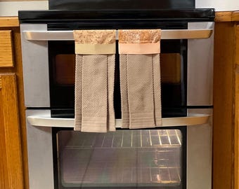 May include: Stainless steel double oven with a black top and two oven doors. The oven has two beige towels hanging on the top door handles.
