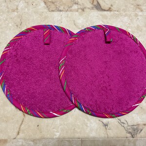 May include: Two round pink pot holders with a colorful striped trim. The pot holders have a loop handle.