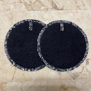 May include: Two round black pot holders with a white paisley border and a small loop for hanging. The pot holders are made of a soft, absorbent material, perfect for protecting surfaces from heat.
