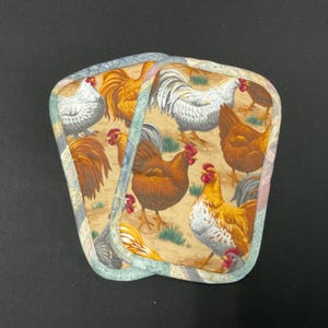 May include: Two fabric pot holders with a repeating pattern of chickens and roosters in various colors. The background is a tan color with green grass. The edges are trimmed with a striped fabric.