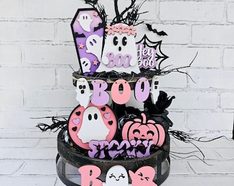 Könnte beinhalten: Ein zweistufiger Holz-Etagere, der mit Halloween-Dekorationen geschmückt ist. Die Etagere zeigt einen rosa-violetten Geist, einen Kürbis, einen schwarzen Kessel und ein Banner mit der Aufschrift "BOO".
