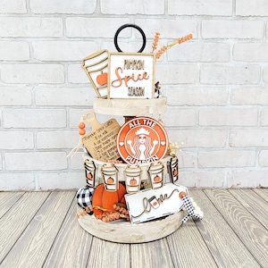 以下が含まれることがあります： 秋をテーマにしたアイテムで飾られた3段の木製トレイ。パンプキン・スパイス・ラテのサイン、ラブのサイン、そして「All the Pumpkin」と書かれたサインがあります。