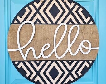 May include: A round wooden door hanger with a black and white geometric pattern. The word "hello" is written in white cursive lettering on a brown wooden background.
