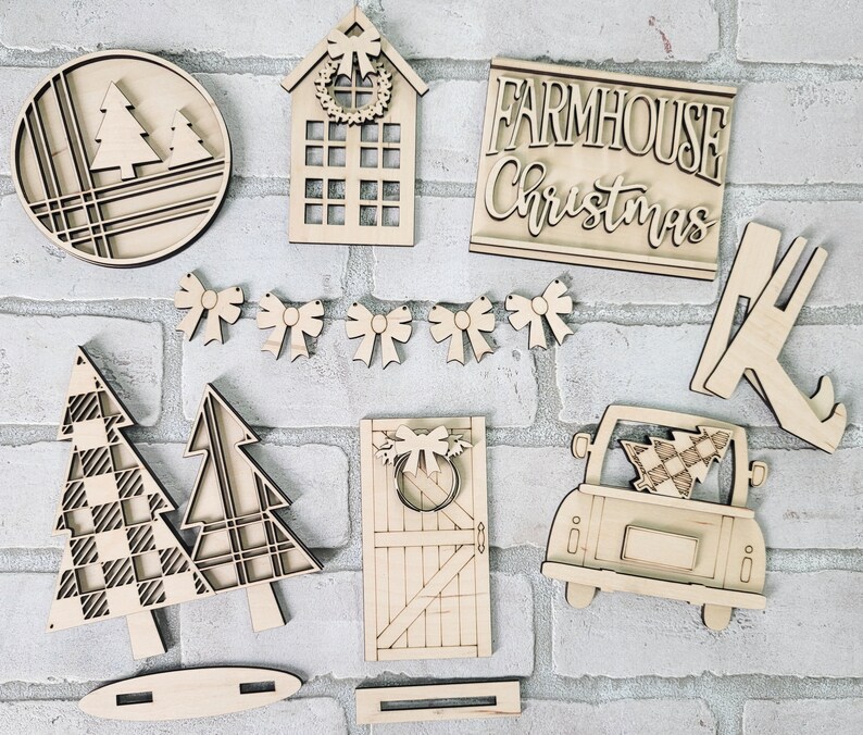 May include: Wooden craft supplies for a farmhouse Christmas theme. The set includes a sign that says "Farmhouse Christmas", a house with a wreath, a tree, a truck with a tree, a door with a wreath, and a set of bows.