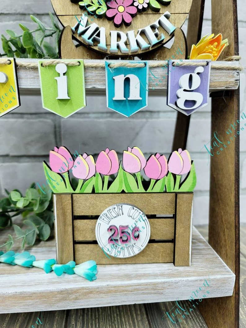 May include: A wooden crate with a sign that says "Fresh Cut Tulips 25&cent;" and a bunch of pink tulips. The crate is sitting on a wooden shelf with a banner that says "Spring" hanging above it.