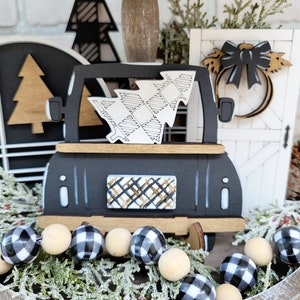 May include: Black and white checkered wooden bead garland with a black wooden truck carrying a white and black checkered Christmas tree. The truck has a black and white checkered window and a gold and black checkered back window. The truck is sitting on a wooden barrel with green pine branches.