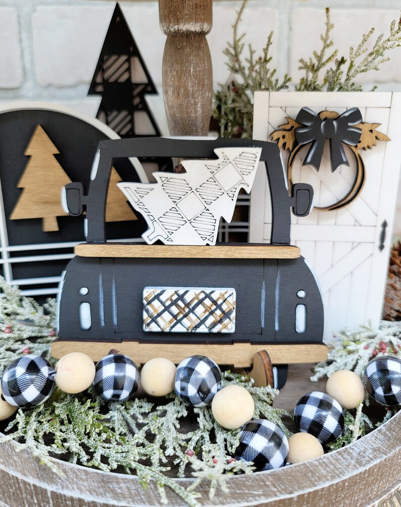 May include: Black and white checkered wooden bead garland with a black wooden truck carrying a white and black checkered Christmas tree. The truck has a black and white checkered window and a gold and black checkered back window. The truck is sitting on a wooden barrel with green pine branches.