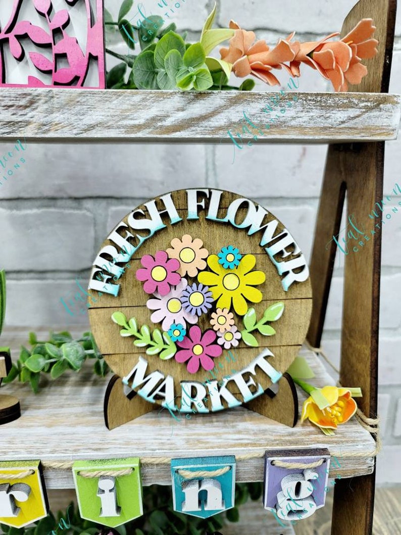 May include: A wooden sign with the words "Fresh Flower Market" in white letters. The sign is decorated with colorful flowers and green leaves. The sign is on a wooden stand.