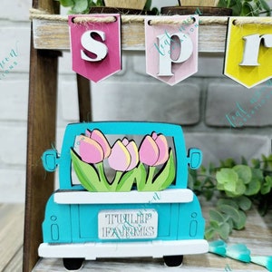 May include: A teal blue wooden truck with a white bed and white wheels. The truck is carrying a bouquet of pink and yellow tulips. The truck has a sign that reads "TULIP FARMS".