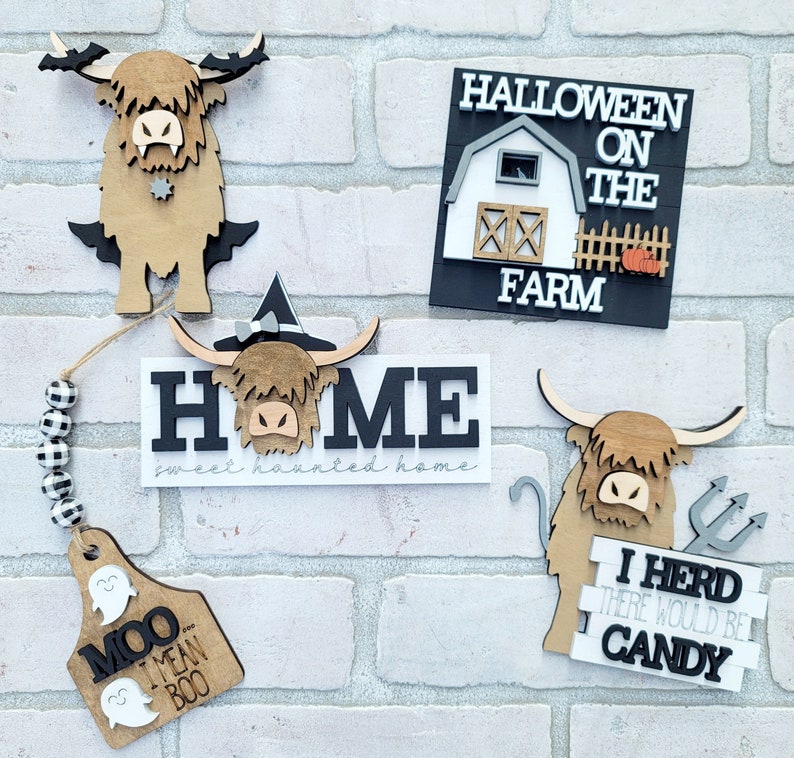 May include: A set of five Halloween-themed wooden signs featuring a highland cow design. The signs say "Home sweet haunted home", "Halloween on the farm", "Moo I mean Boo", and "I herd there would be candy".
