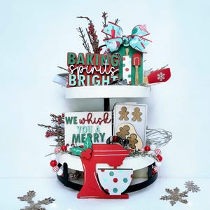 May include: A two-tiered decorative tray with Christmas-themed baking decorations. The top tier has a sign that reads "Baking Spirits Bright" and a bow. The bottom tier has a red mixer and a sign that reads "We Whisk You a Merry".