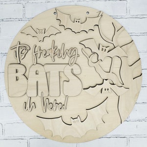 Op de afbeelding: Een rond houten bord met de tekst "It's Freaking Bats in Here!" en meerdere vleermuis uitsnijdingen. Het bord is geschilderd in een natuurlijke houtkleur.
