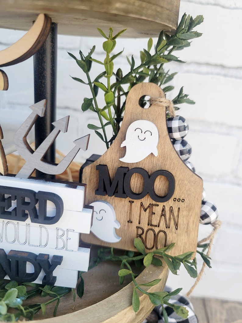 May include: A tiered wooden tray decorated with a ghost, a wooden sign that says "MOO I MEAN BOO", and black and white buffalo check ribbon.