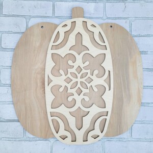 May include: A wooden pumpkin cutout with a decorative, intricate design. The pumpkin is made of two pieces, one with the design and the other a solid piece.