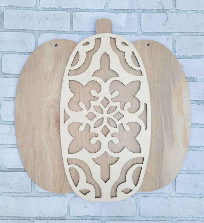 May include: A wooden pumpkin cutout with a decorative, intricate design. The pumpkin is made of two pieces, one with the design and the other a solid piece.