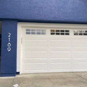 May include: A white garage door with a blue wall and the house number 2189 on the side.