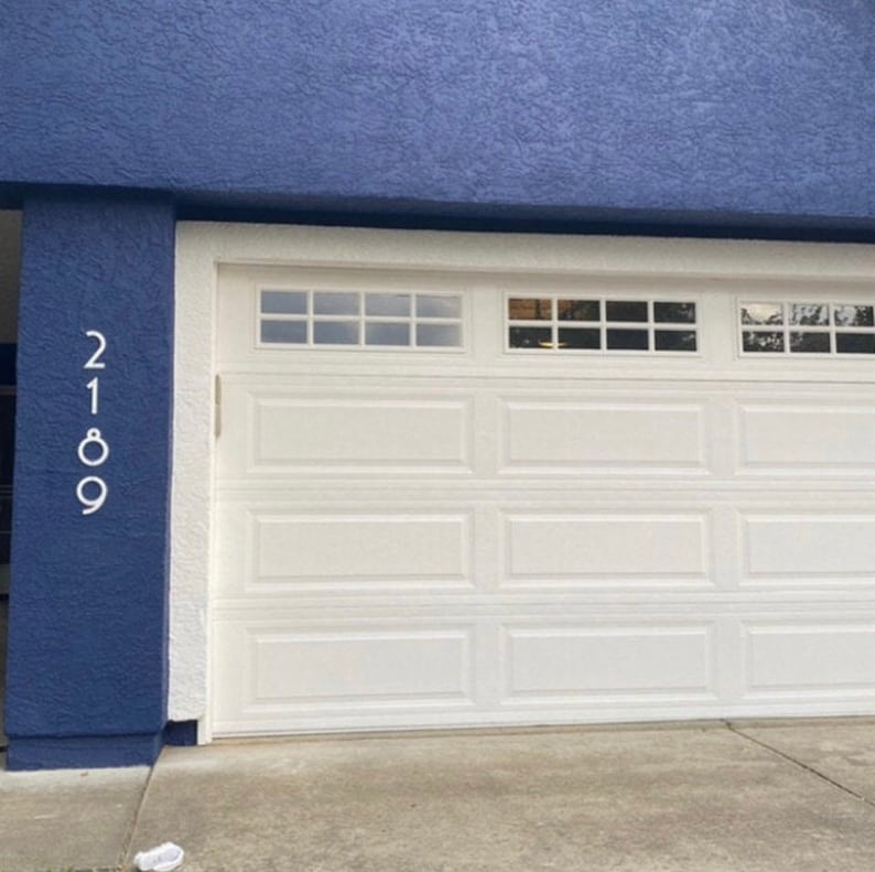 May include: A white garage door with a blue wall and the house number 2189 on the side.