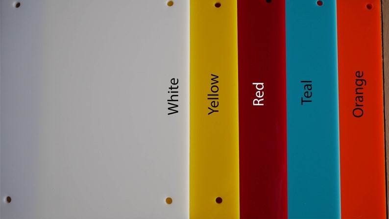 May include: A collection of colorful rectangular acrylic sheets in white, yellow, red, teal, and orange. Each sheet has a hole in the top corners and the color name printed vertically. The sheets are arranged side by side.