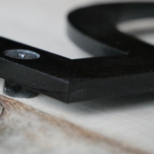 May include: Close-up of a black metal house number with a screw attaching it to a surface.