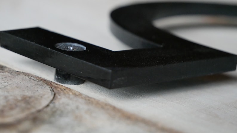 May include: Close-up of a black metal house number with a screw attaching it to a surface.