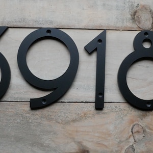 May include: Black metal house numbers 3918 mounted on a wooden surface.