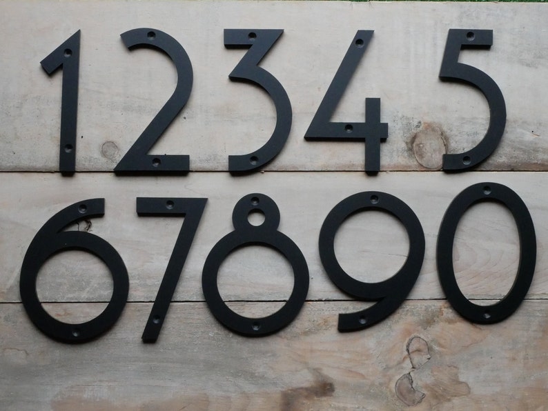 May include: Black metal house numbers 1 through 9. The numbers are attached to a wooden surface.