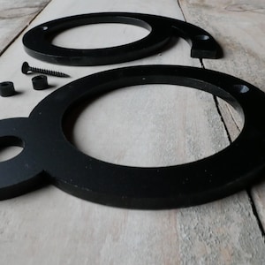 May include: Two black metal house numbers, shaped like the number eight, with mounting hardware. The numbers are on a wooden surface.
