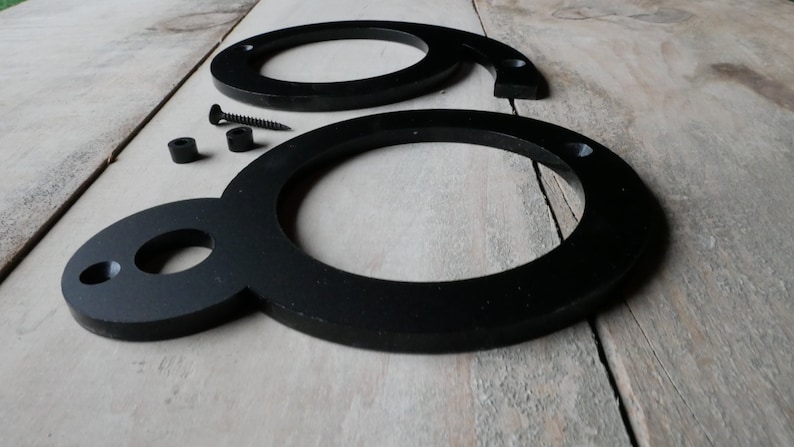 May include: Two black metal house numbers, shaped like the number eight, with mounting hardware. The numbers are on a wooden surface.