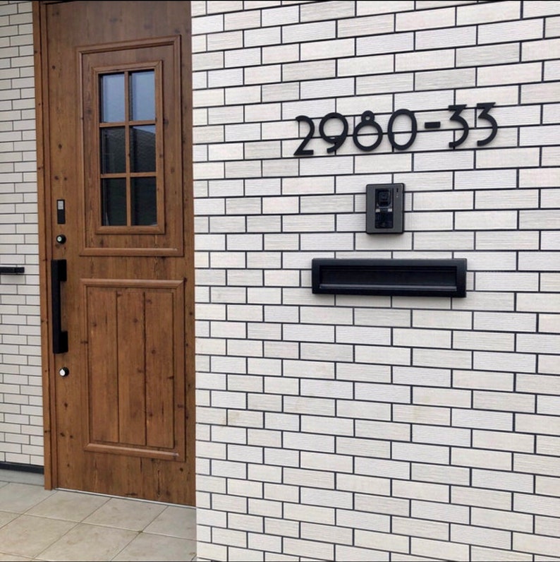 May include: A white brick building with a wooden door and a black mailbox. The house number is 2980-33.