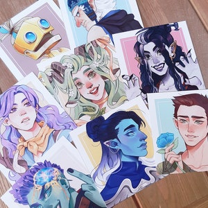 May include: A selection of art prints displaying vibrant illustrations of fantasy characters. The prints depict diverse characters with distinctive features, such as robots and elves. Each print has a white border and is set against a light background.