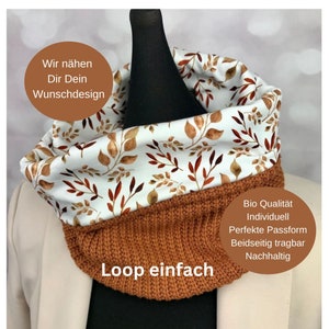 Op de afbeelding: Een bruine gebreide loopsjaal met een witte voering van stof met een bruin en gouden bladmotief. De sjaal is omkeerbaar en heeft de tekst "Loop einfach" op de gebreide kant. De tekst "Wir nähen Dir Dein Wunschdesign" staat in de linkerbovenhoek van de afbeelding. De tekst "Bio Qualität Individuell Perfekte Passform Beidseitig tragbar Nachhaltig" staat aan de rechterkant van de afbeelding.