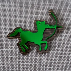 May include: A green wooden cutout of a centaur with a bow and arrow. The cutout is on a gray textured background.