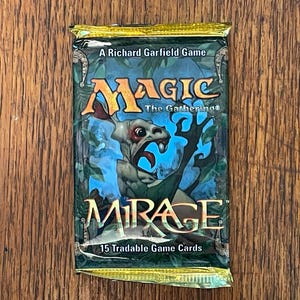 May include: A sealed Magic The Gathering Mirage booster pack featuring a green and blue jungle illustration with a central creature graphic. The packaging displays the text A Richard Garfield Game, Magic The Gathering, Mirage, and 15 Tradable Game Cards.