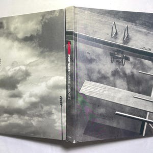 May include: A hardcover book titled "Olympia Portraits" by Annie Leibovitz. The cover features a black and white photograph of a diving board and pool. The spine of the book is black with white text.