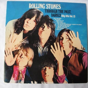 May include: Album cover for The Rolling Stones' "Through the Past, Darkly (Big Hits Vol. 2)". The cover features a group photo of the band members with their hands up. The background is a vibrant blue.