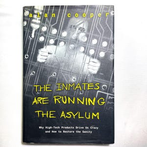 May include: A book cover with the title "THE INMATES ARE RUNNING THE ASYLUM" in yellow text. The author's name, "alan cooper", is at the top. The cover features a grayscale image of a person behind a circuit board design.