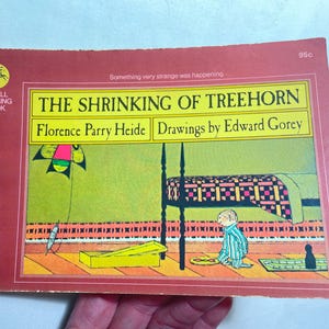 May include: A vintage paperback book titled "The Shrinking of Treehorn" by Florence Parry Heide, with drawings by Edward Gorey. The cover features a colorful illustration of a child in a striped outfit, a bed, and a kite. The book is a Dell Yearling Book.
