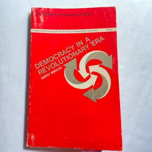 May include: A red book titled "DEMOCRACY IN A REVOLUTIONARY ERA" by Harvey Wheeler. The cover features a gray and white arrow design. The book is a Center Occasional Paper published by the Center for the Study of Democratic Institutions.