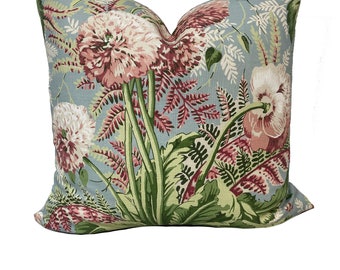 Può includere: Un cuscino decorativo con un motivo floreale che presenta fiori rosa e bianchi, foglie verdi e fogliame simile a felci su uno sfondo blu chiaro.