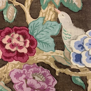 May include: A brown fabric with a floral pattern featuring pink, red, blue, and green flowers. A white bird with green markings is perched on a branch.