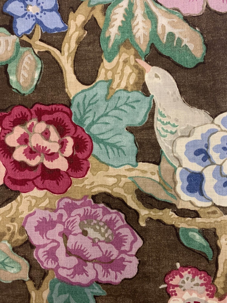 May include: A brown fabric with a floral pattern featuring pink, red, blue, and green flowers. A white bird with green markings is perched on a branch.