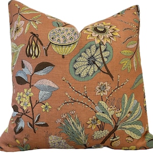 Könnte beinhalten: Ein pfirsichfarbener Kissenbezug mit einem floralen Muster aus grünen Blättern, gelben Blüten und braunen Stielen. Das Muster erinnert an eine botanische Illustration.