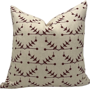 May include: A square cushion with a beige backdrop and a repeating pattern of dark burgundy geometric shapes. The pattern features stylized leaf-like elements connected by lines and dots, creating a symmetrical design.