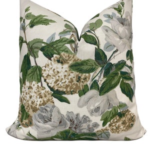 May include: A decorative throw pillow with a floral pattern. The pillow features large, gray and white roses, green leaves, and tan hydrangea blooms against a cream background. The pillow is square and has a soft, inviting appearance.