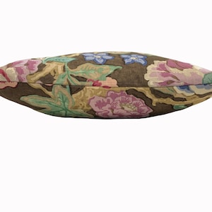 May include: A brown linen pillow with a floral pattern featuring pink, purple, and blue flowers. The pillow is rectangular and has a slightly curved shape.