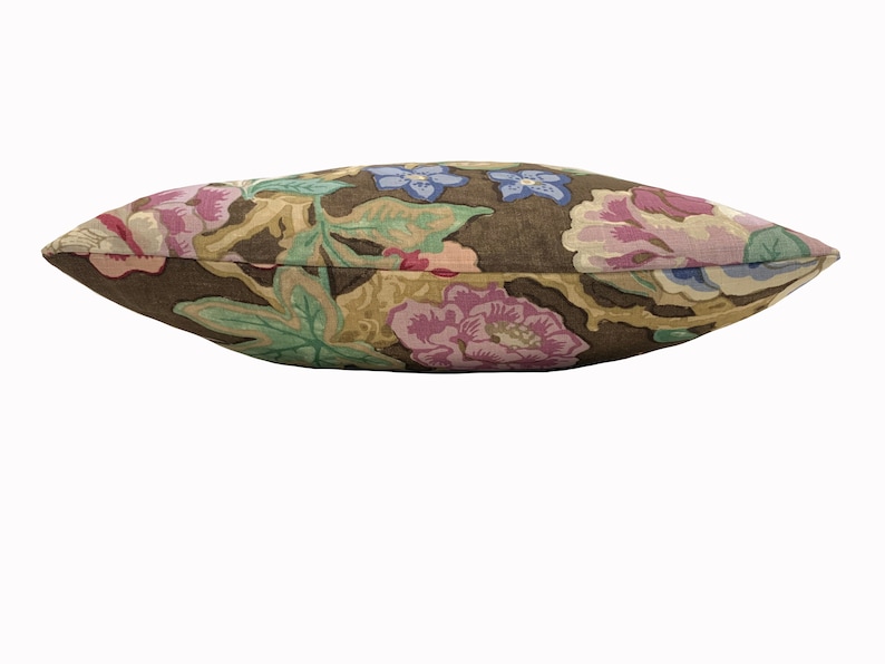 May include: A brown linen pillow with a floral pattern featuring pink, purple, and blue flowers. The pillow is rectangular and has a slightly curved shape.