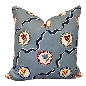 May include: A blue cushion with a repeating pattern of stylised tulips in red, yellow, and blue, surrounded by a white starburst and blue wavy lines.