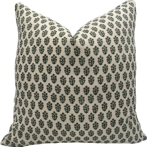 May include: Square decorative pillow with a cream-colored background and a repeating pattern of dark green leaf-like shapes. The pillow has a soft, inviting appearance, suitable for home decor.
